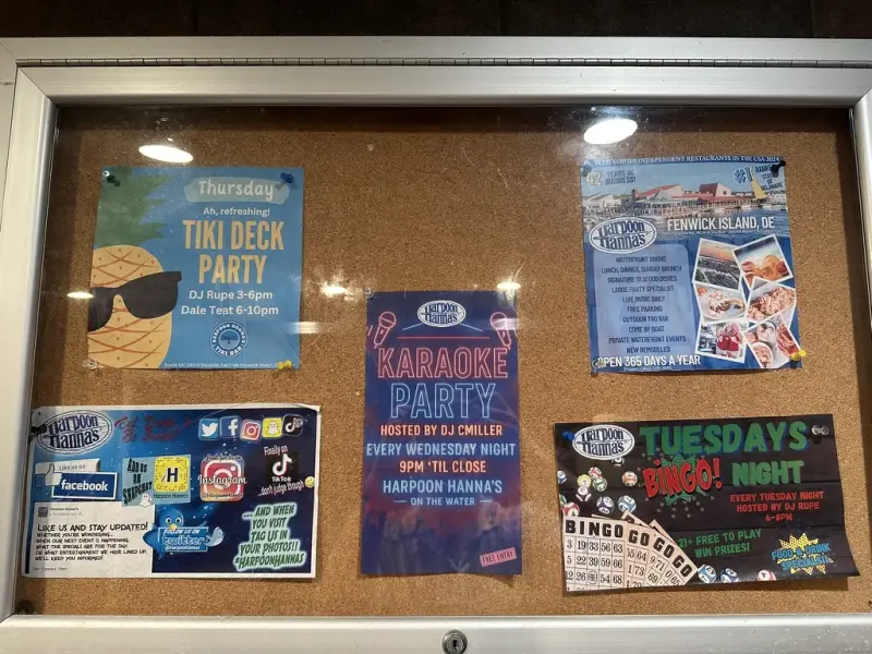 Bulletin board behind glass at Harpoon Hanna's with flyers for a Thursday Tiki Deck Party, a Wednesday Karaoke Party, and Tuesdays Bingo Night